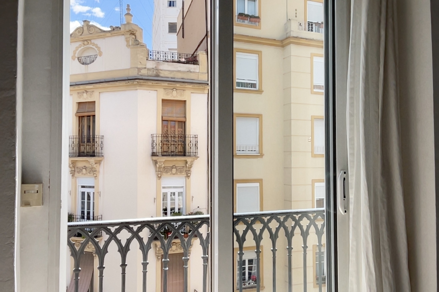 A view of neighboring buildings with ornate balconies is visible through a window with a decorative railing.